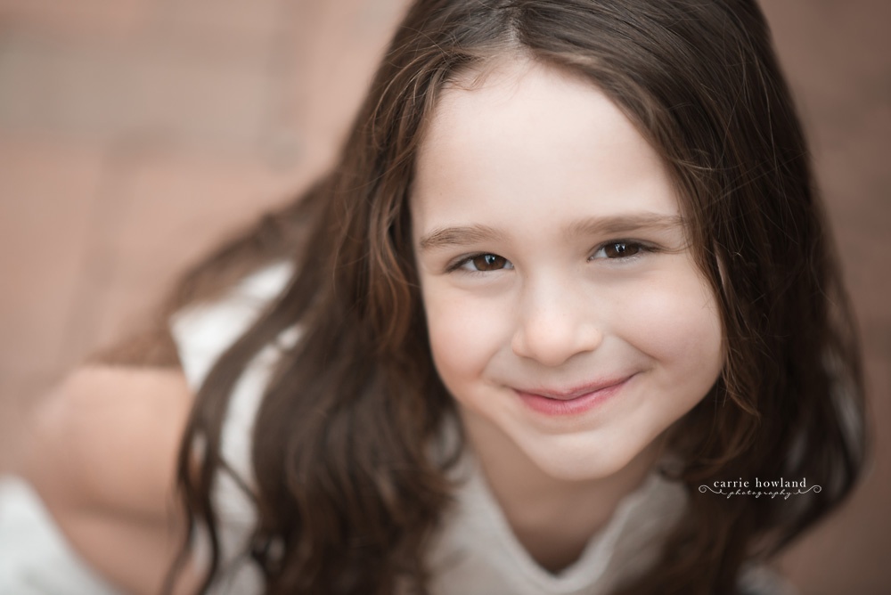 Headshot of dark-haired child with brown eyes seated on path at Davidson College