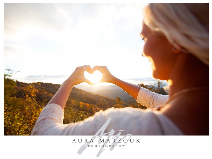 Hands make a heart with a lovely sun backdrop at this Pisgah National Forest engagement session. © Aura Marzouk Photography, Greensboro Wedding Photographer