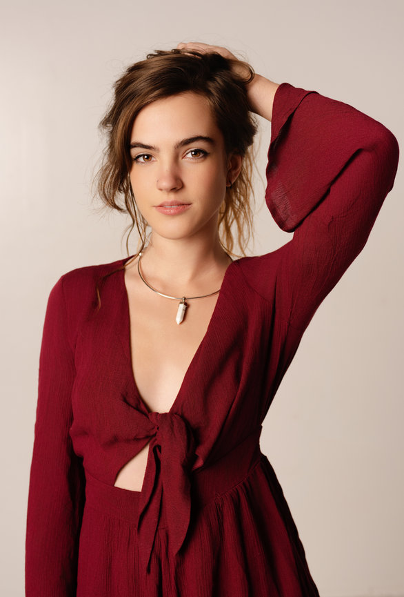 Woman in a burgundy dress posing with one arm raised in a studio