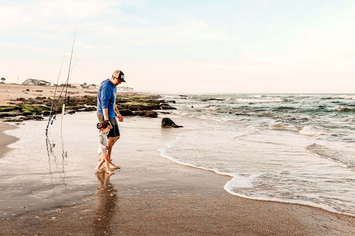 father and daughter walking into the waves on a Florida beach, fishing poles in background