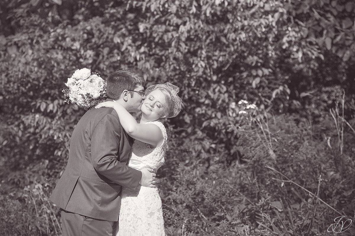 black and white photo of groom kissing bride on cheek