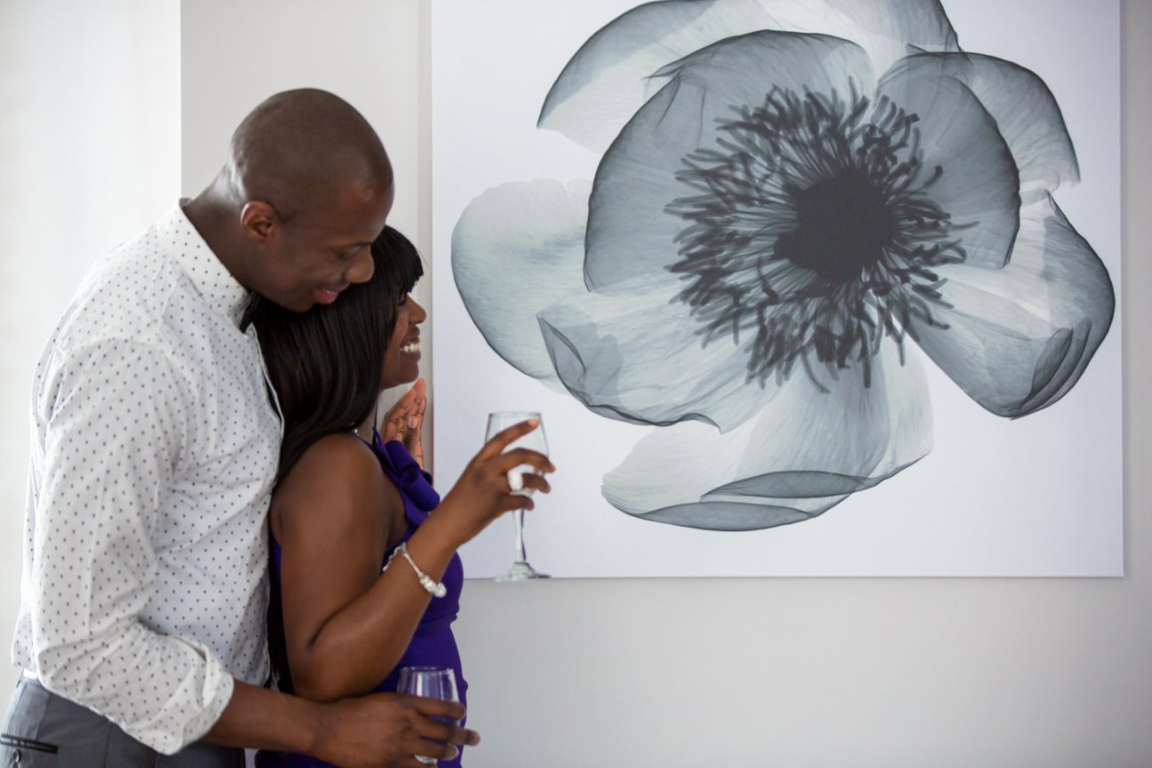 Couple laughing and holding wine glasses near a large black-and-white floral painting.