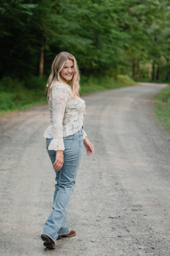 Senior in lace top and jeans walking on a forest road