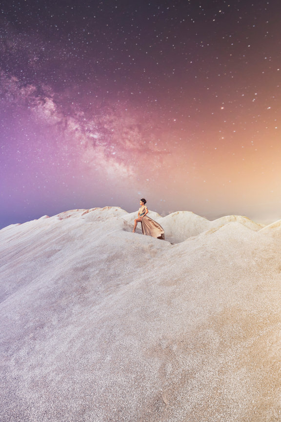 Woman in a flowing gown walking on sandy hills under a starry sky with a vibrant gradient backdrop.