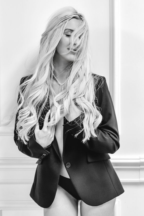 Model in a black blazer poses with long, wavy hair partially obscuring her face, captured in black and white.