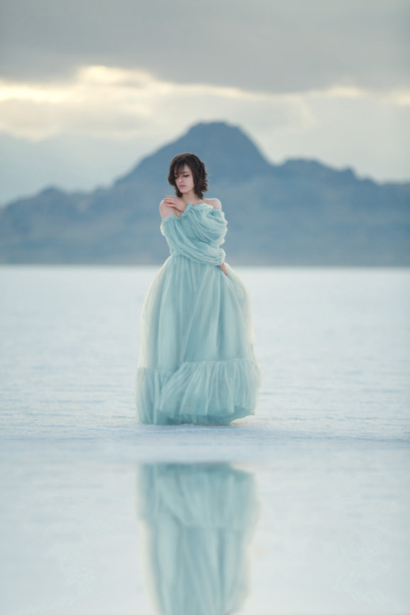 Woman in blue dress standing on a salt flat with mountains in the background