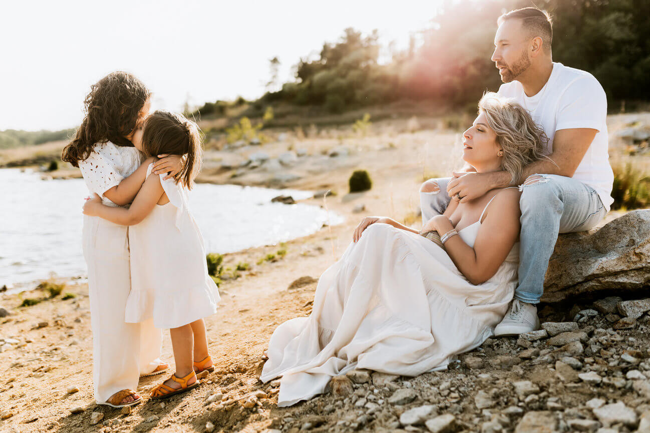 A mother and father sitting on a rocky beach while their daughters hug beside them in Hunterdon County, New Jersey.