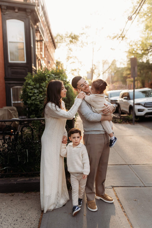 A family dressed in neutrals standing on a street corner in Jersey City at sunset during their New Jersey family photography session.