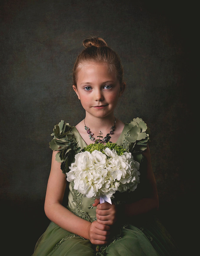 A blond haired girl in a green dress holds a bunch of white hyrangeas.