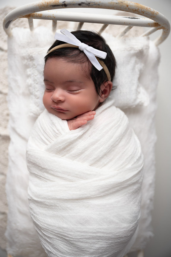 Newborn baby girl sleeping wrapped up in a tiny bed and white headband