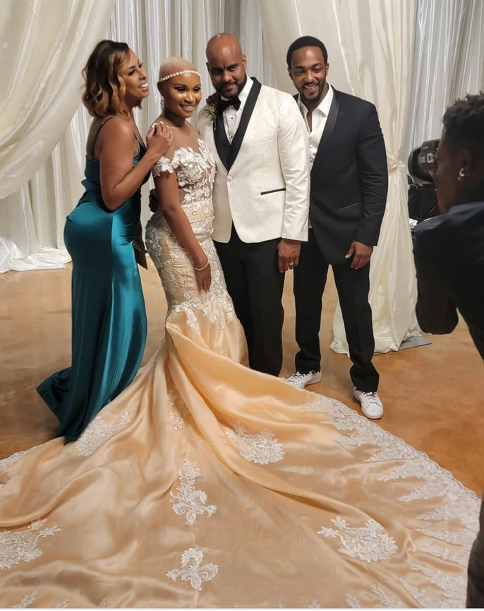 Bride in a flowing gown poses with three guests in formal attire for a photo against a backdrop of draped curtains.