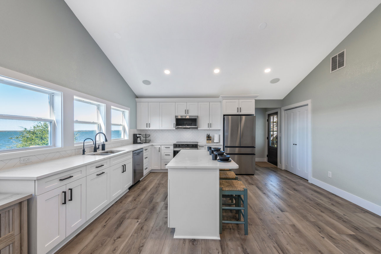 Modern kitchen with white cabinets, stainless steel appliances, an island with seating, and large windows displaying a water view.