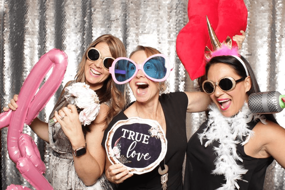 Three women in a photo booth wearing party accessories