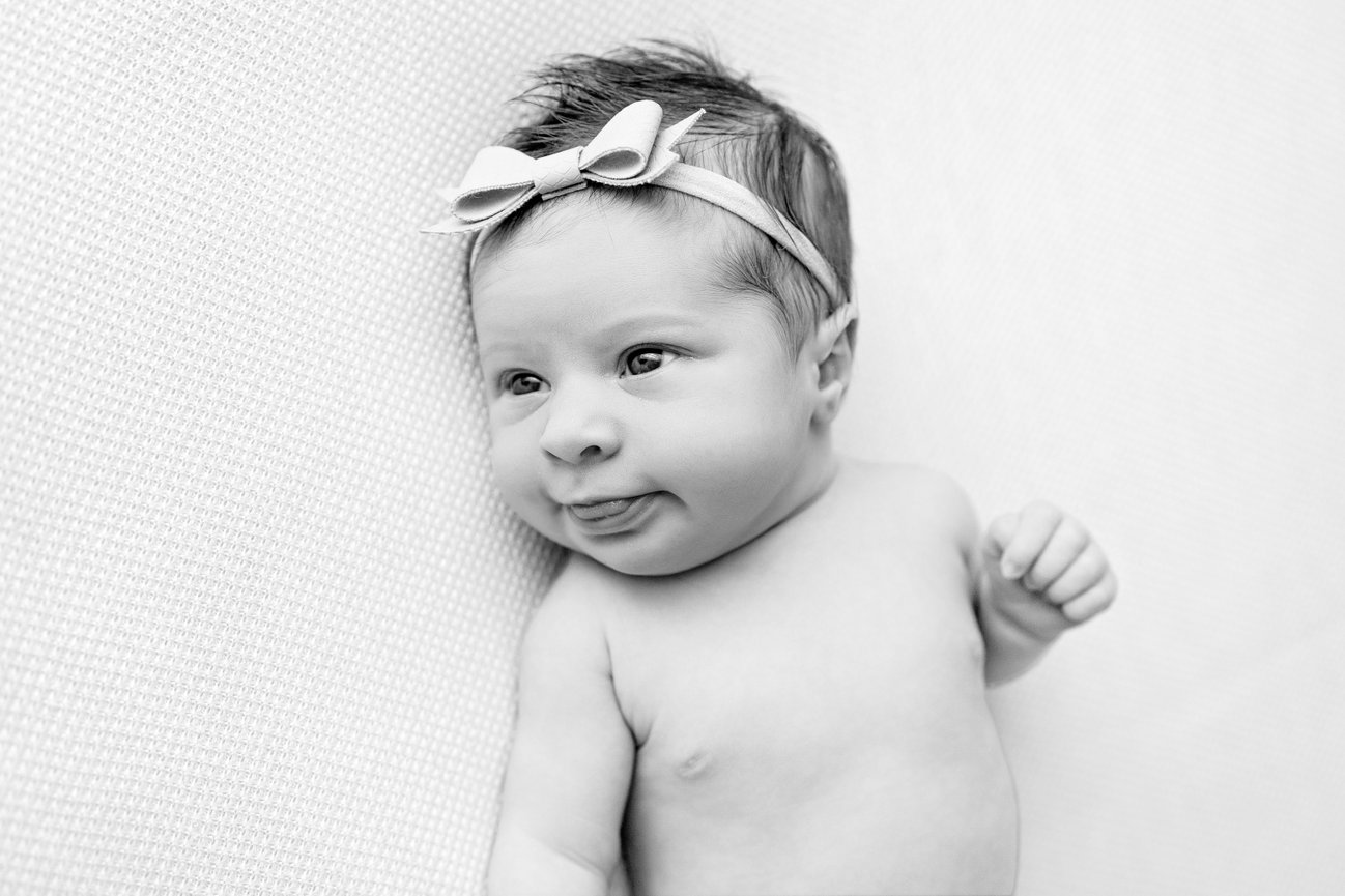 Black and white close-up of a baby wearing a headband with a bow, lying on a soft blanket