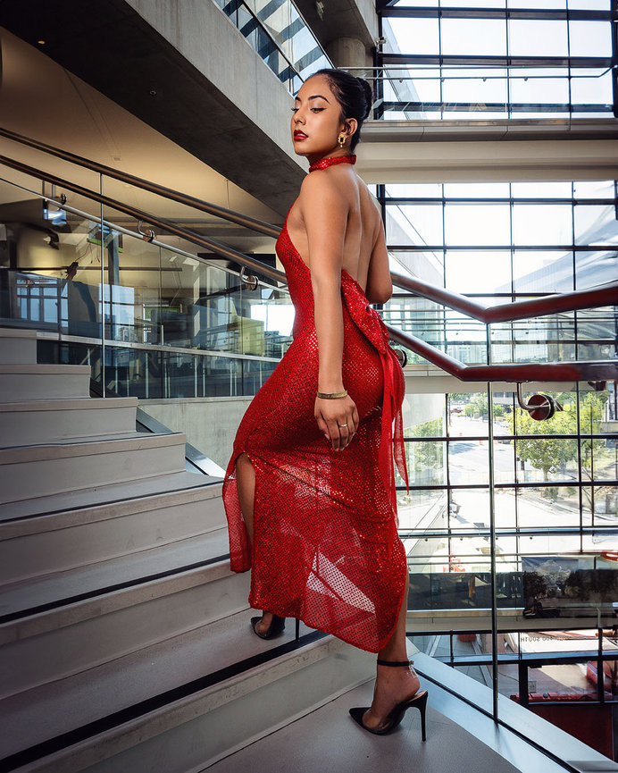 Latina model in an elegant red dress ascending modern glass stairs inside the Salt Lake City Library, showcasing fashion and sophistication. Captured by Tre Nelson Photo, highlighting architectural beauty and glamorous style.