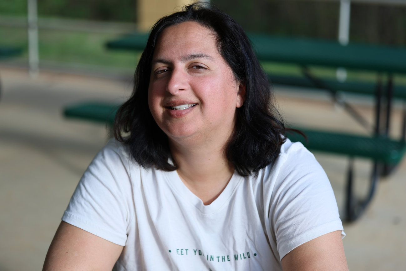 Smiling woman in a white shirt seated outdoors.