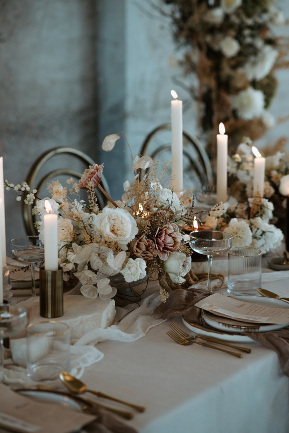 Garden-inspired neutral table scape details with a centerpiece and a collection of place setting aswell as an arch in the backgroud