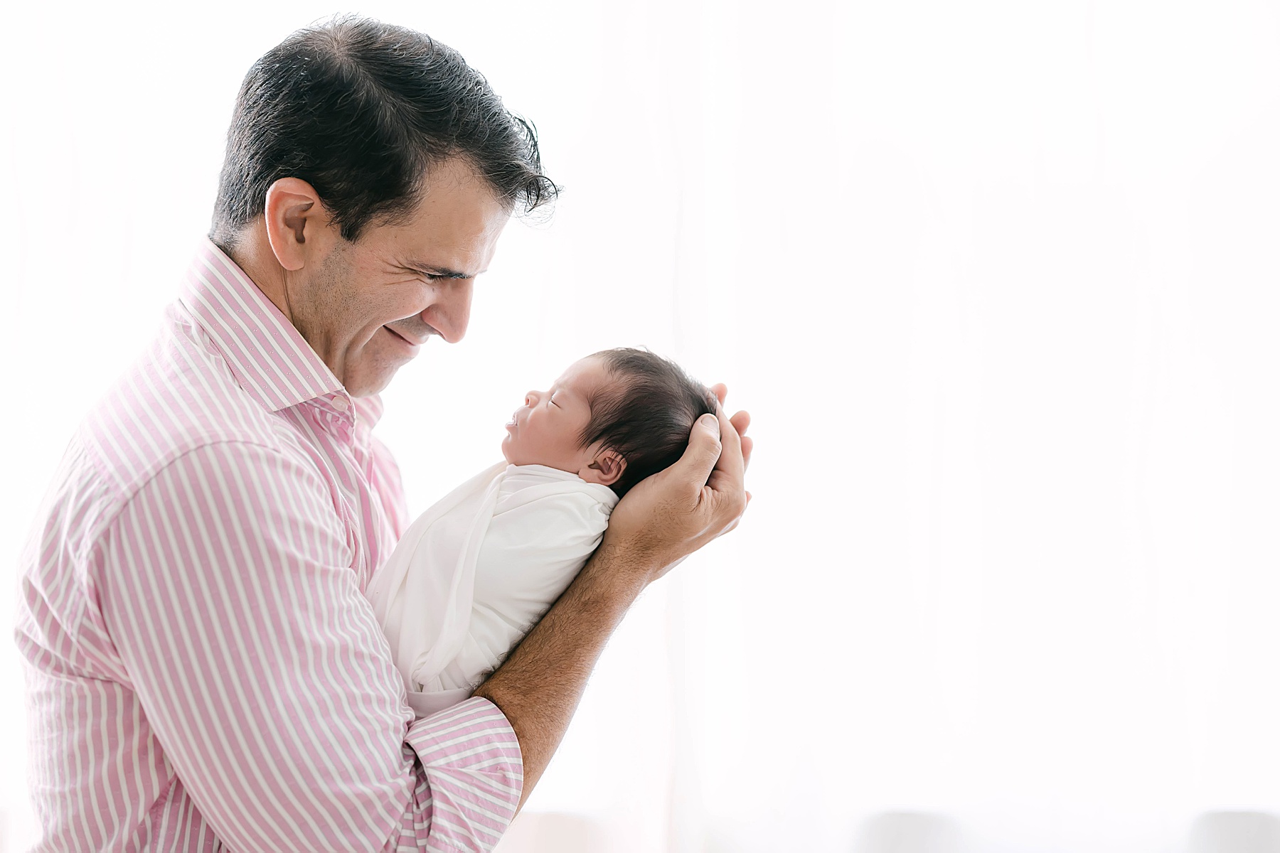 dad holding newborn baby in front of window