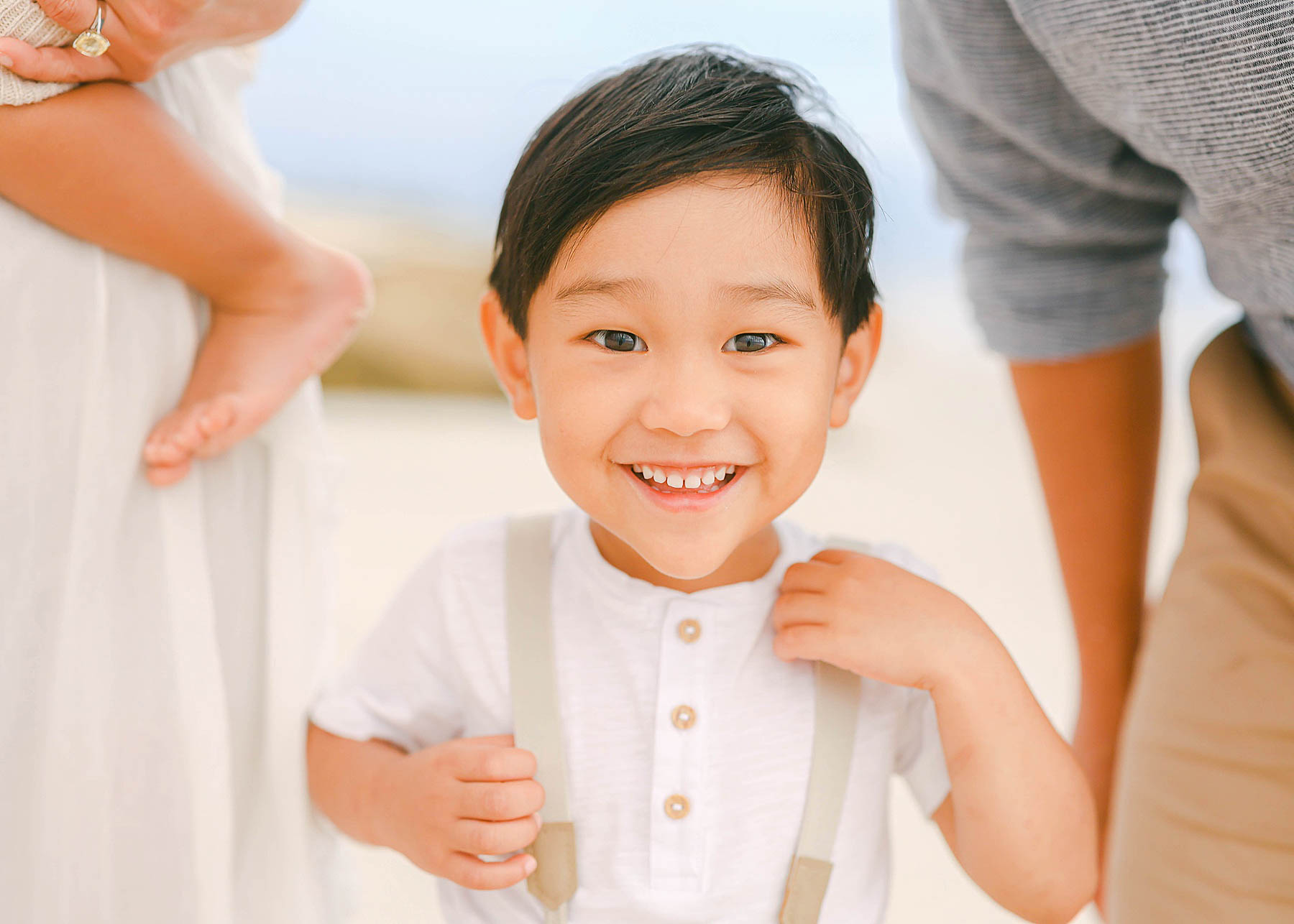 little boy in suspenders at the beach smiling