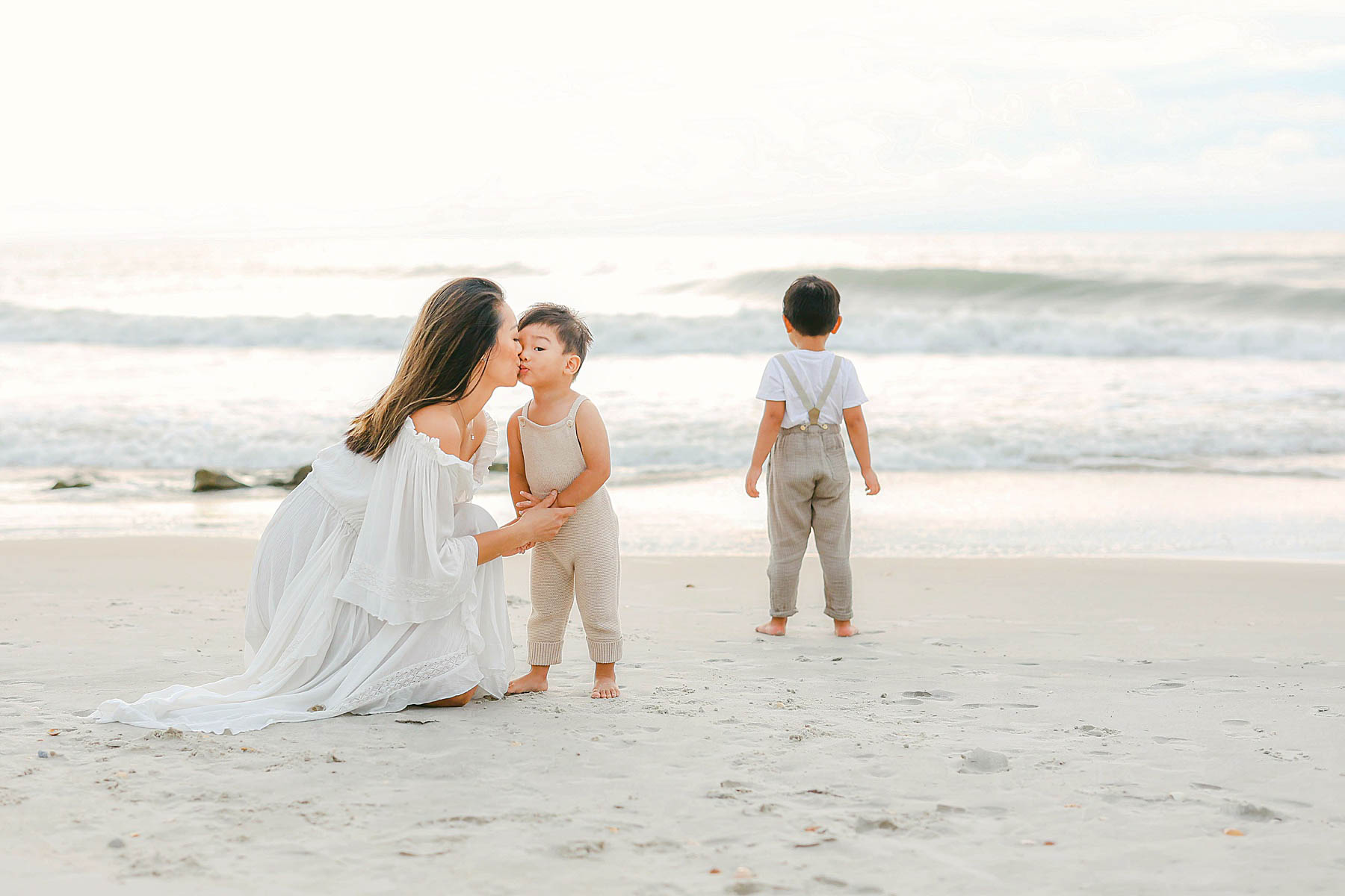 mom kissing baby boy on the beach wearing white dress