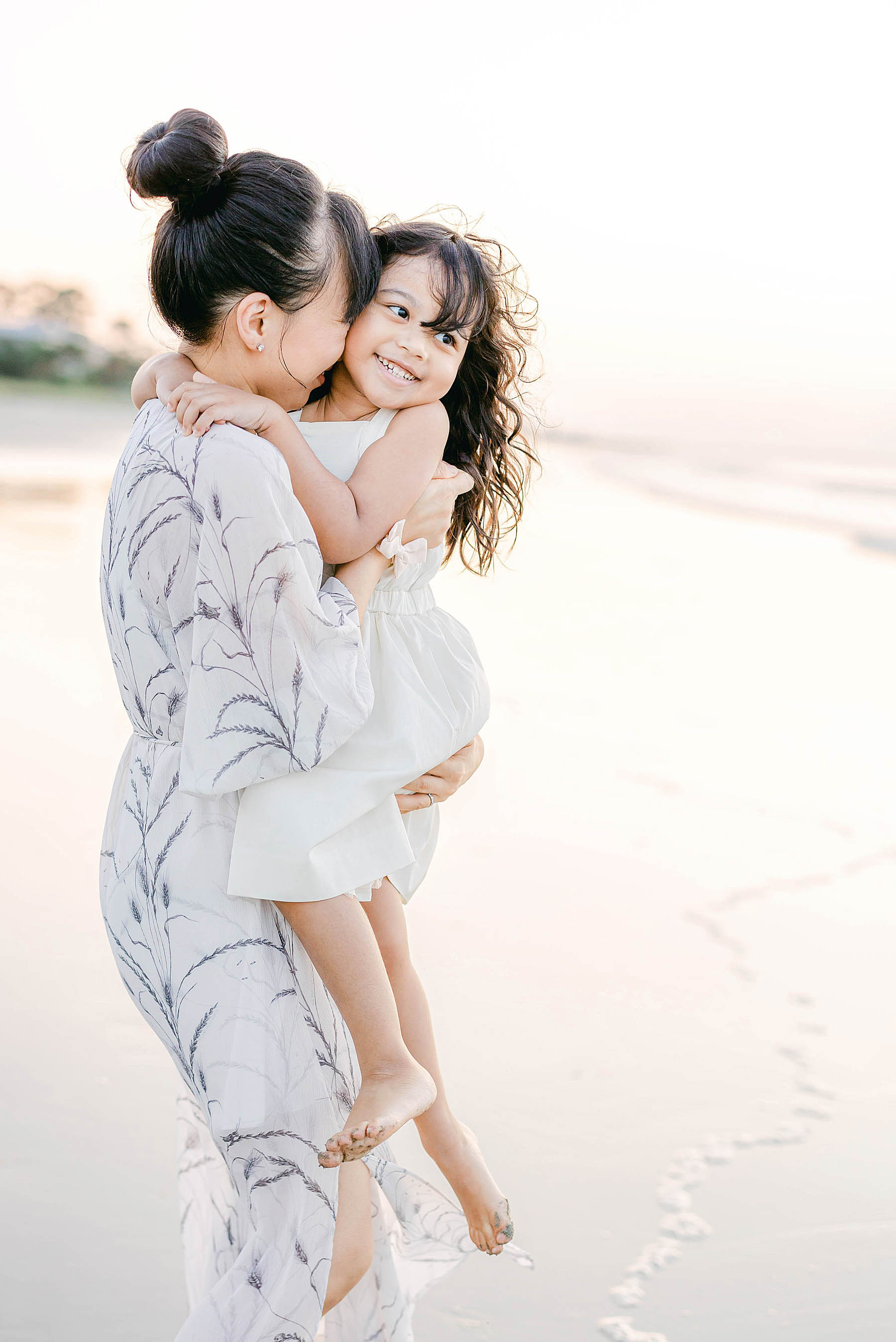 woman snuggling little girl in a long dress at sunrise