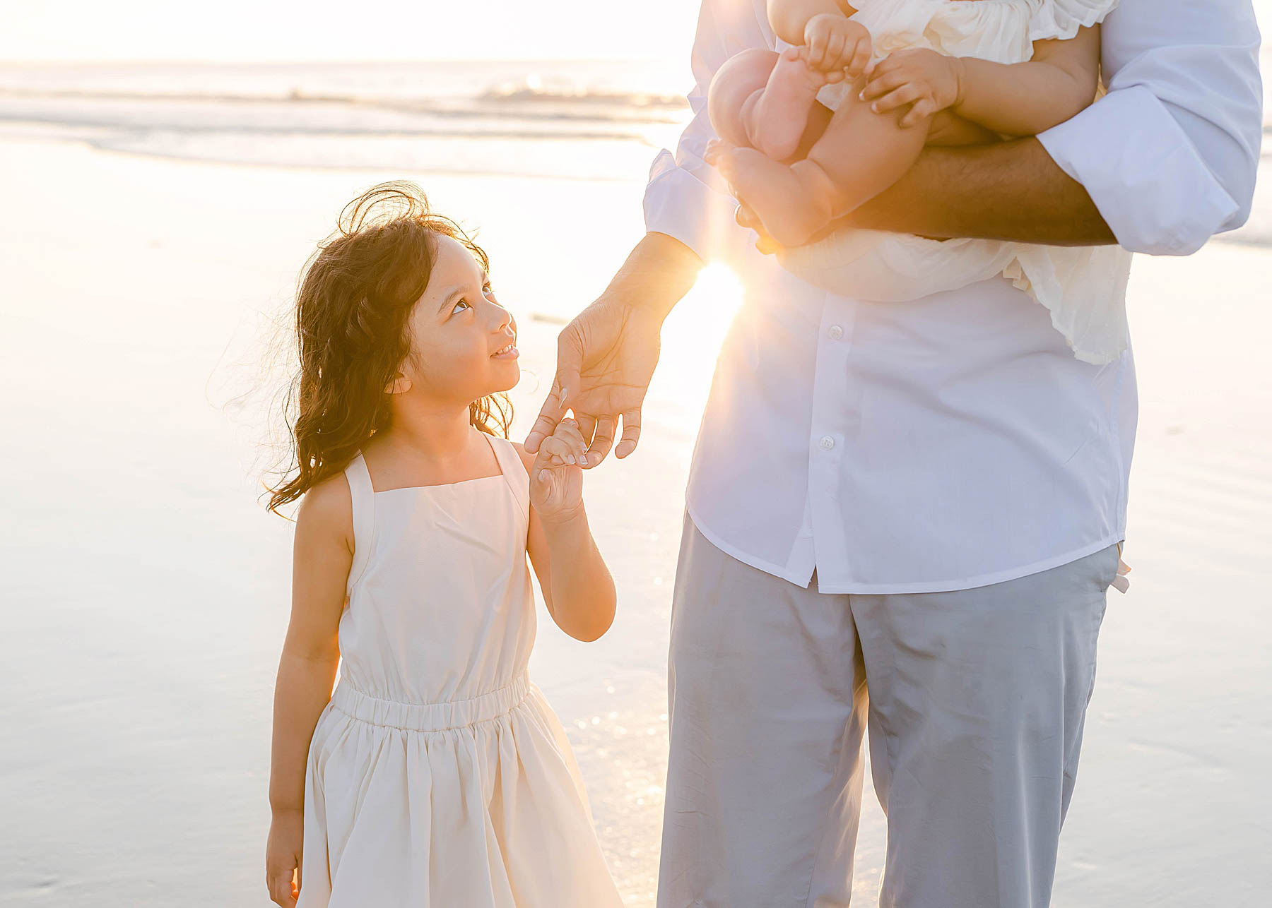 little girl in white dress staring at dad with sun behind her