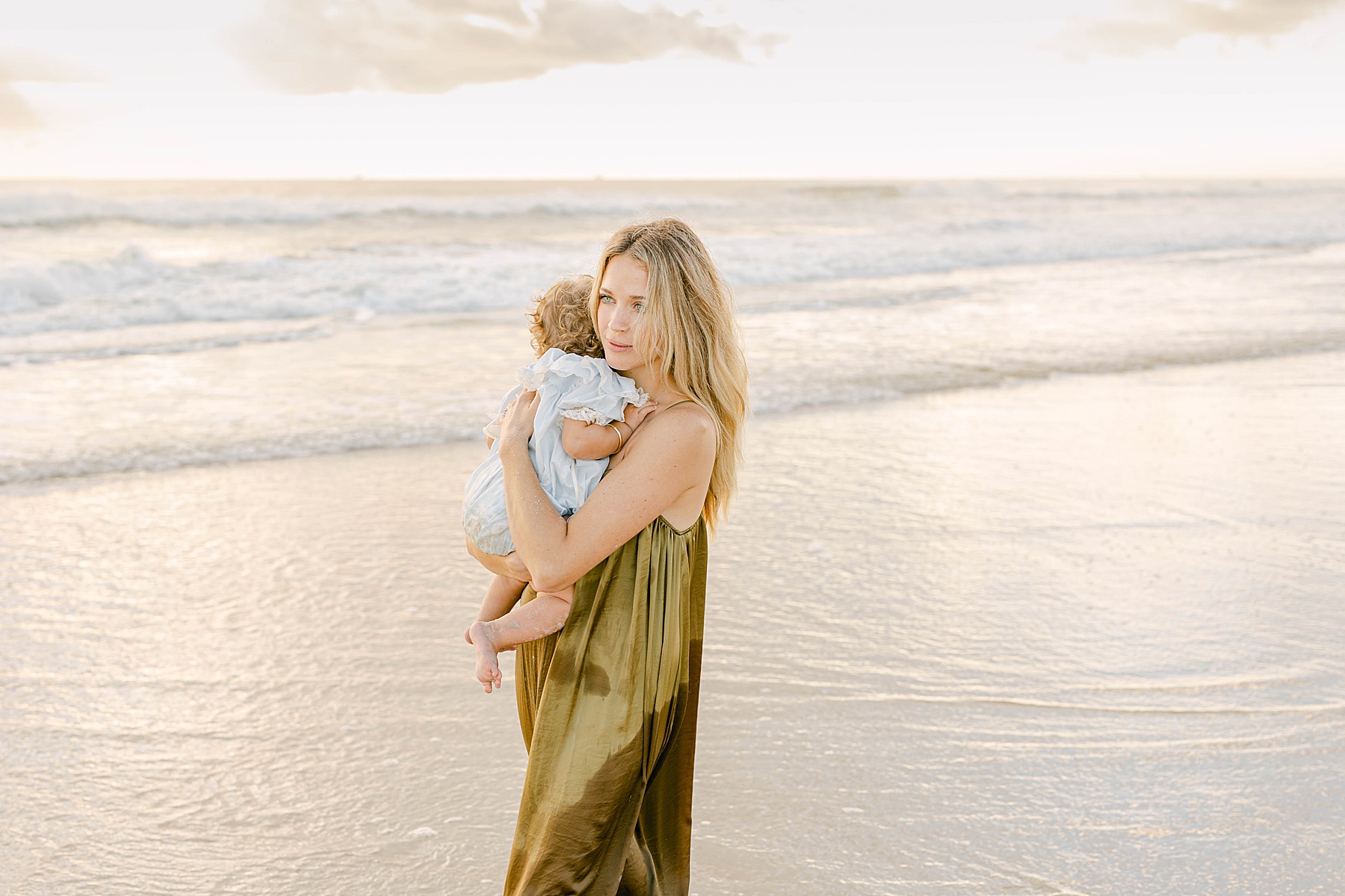 woman in green dress in the water at the beach with baby