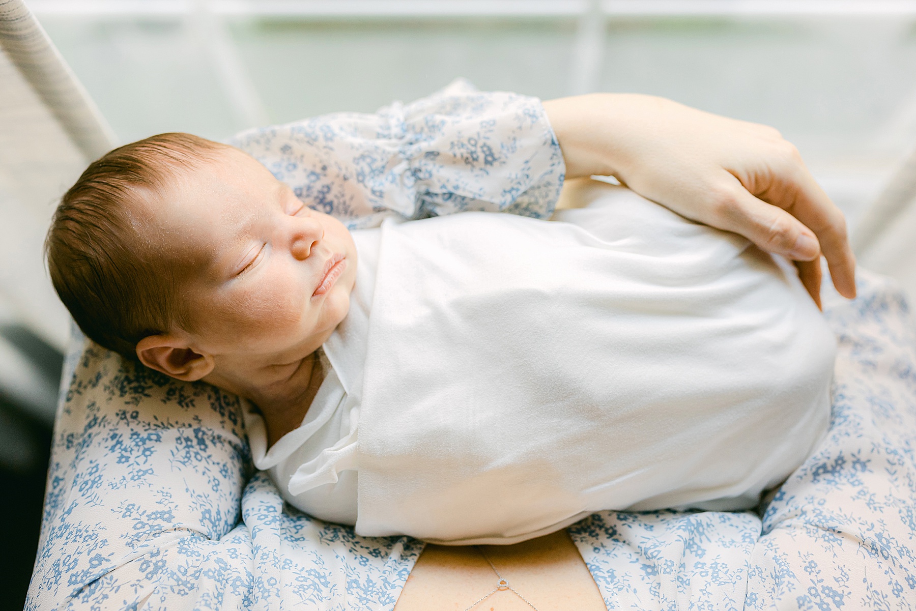 newborn baby in front of window wrapped in a white blanket