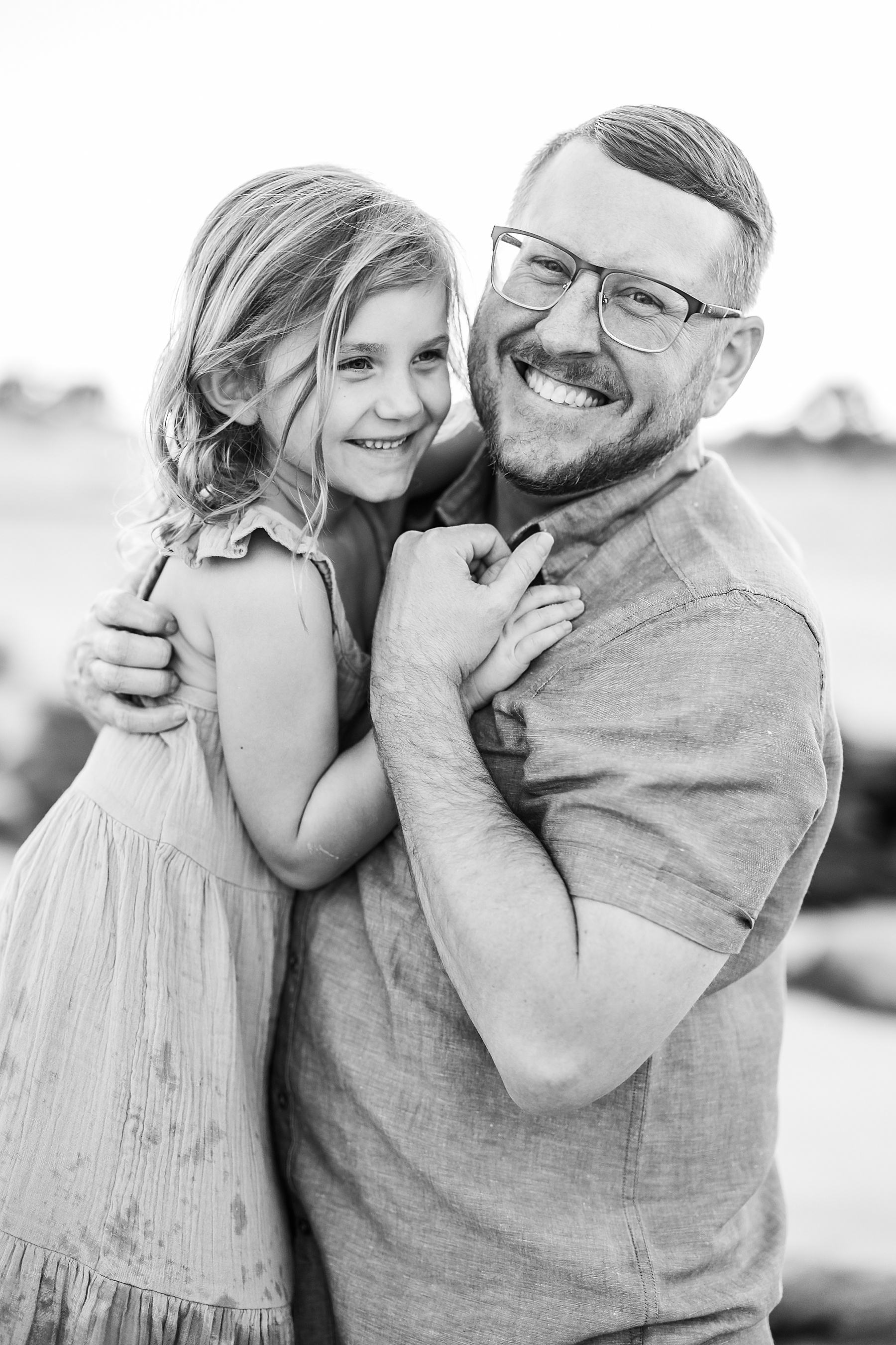 black and white photo of man holding little girl at the beach smiling