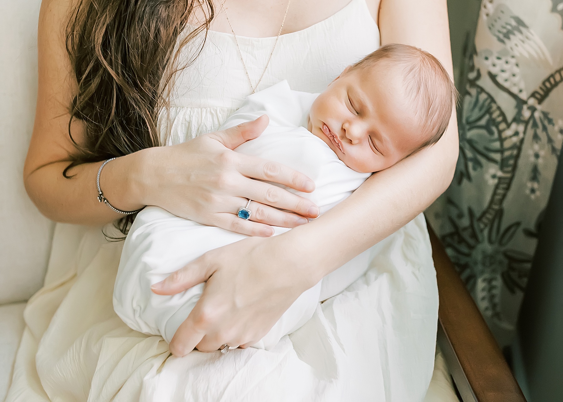 woman wearing blue stone ring holding newborn baby boy wrapped in white blanket