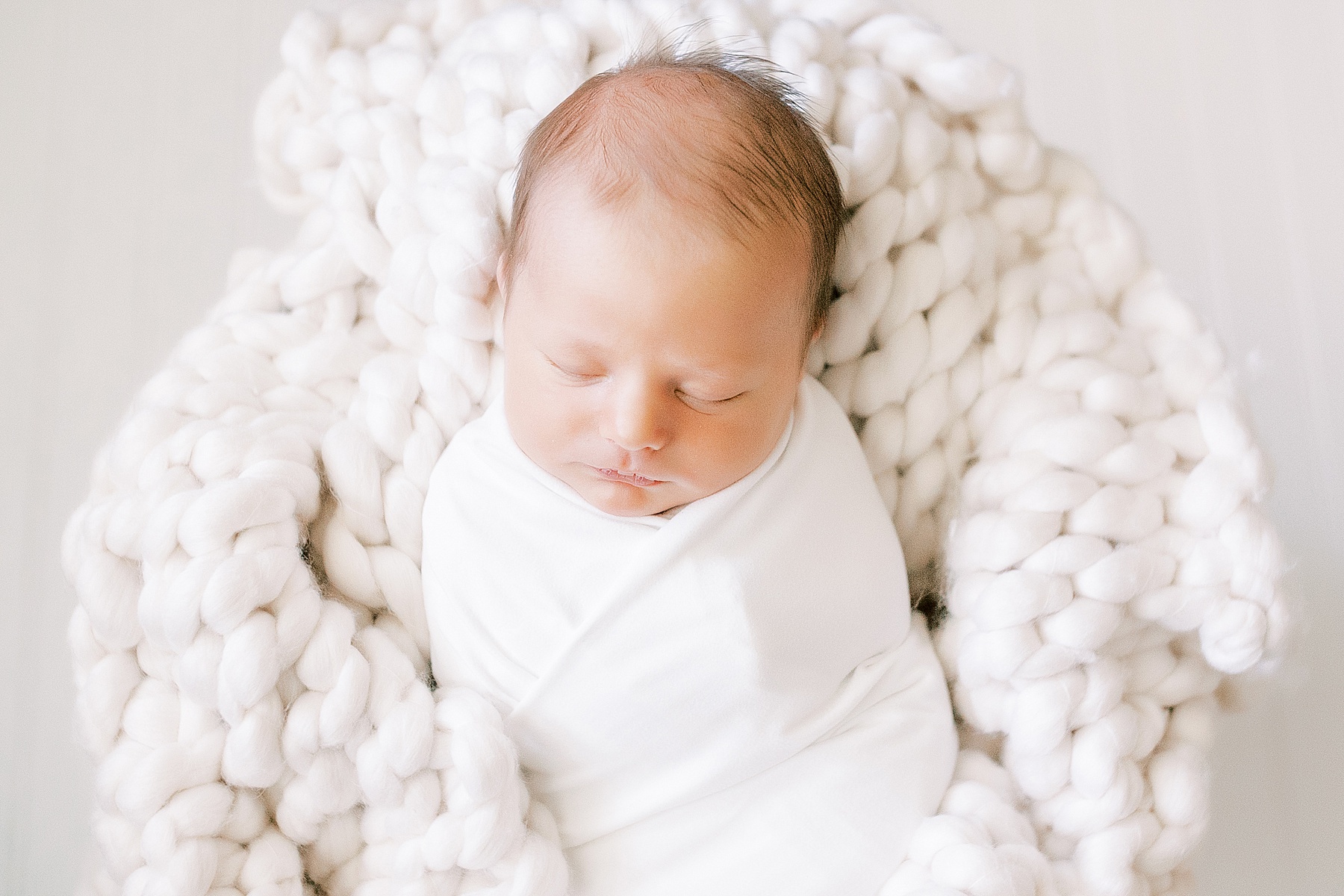 newborn baby boy wrapped in white blanket on chunky knit wool blanket
