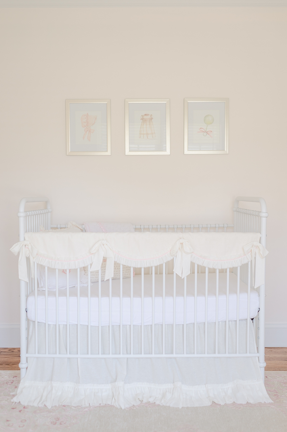 white crib with lace bedding against white wall with framed prints above