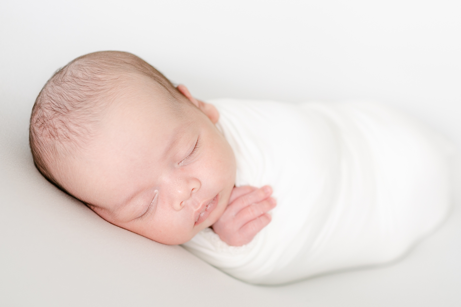newborn baby boy wrapped in white blanket sleeping