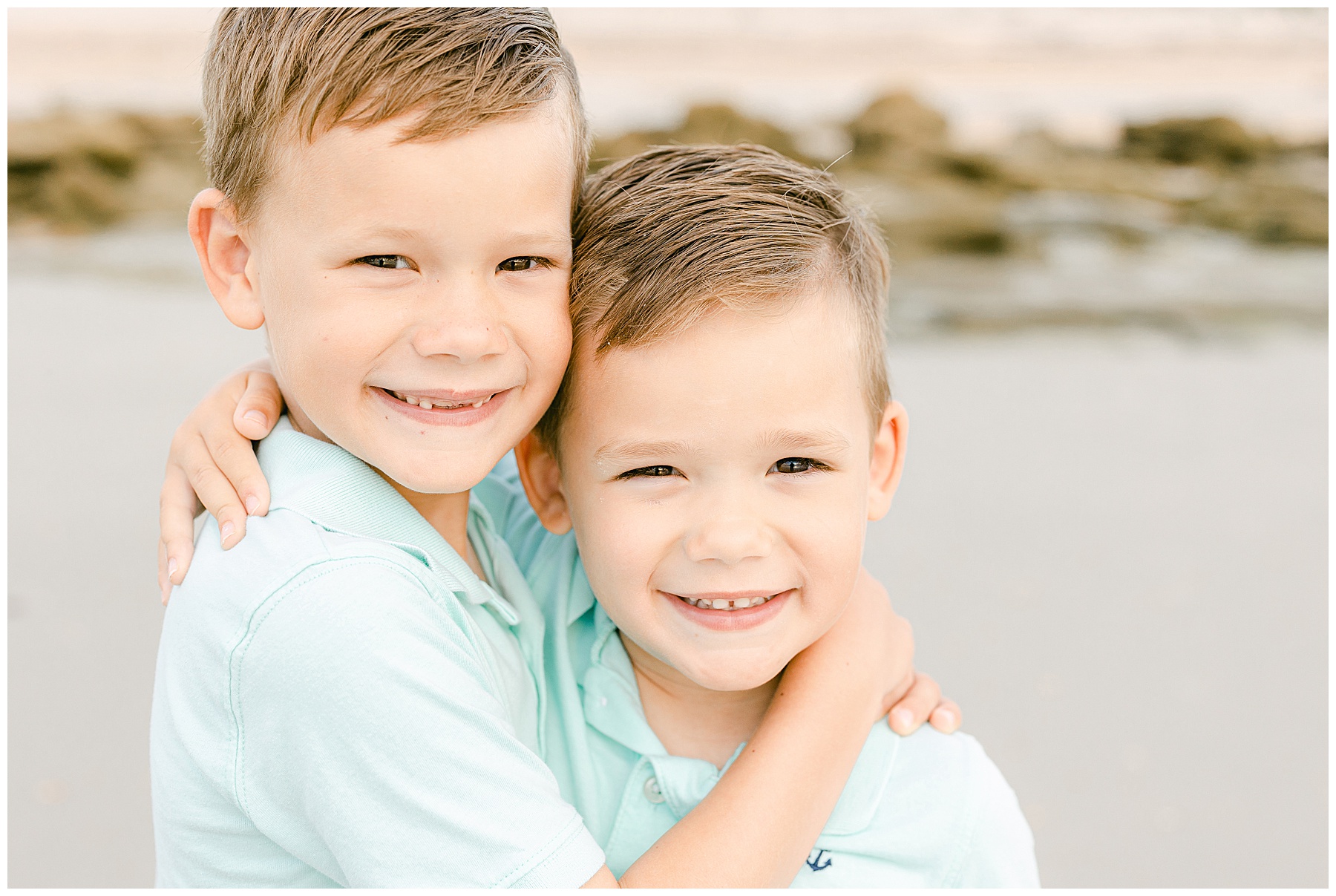 two little boys holding each other on the beach at sunrise wearing aqua blue shirts