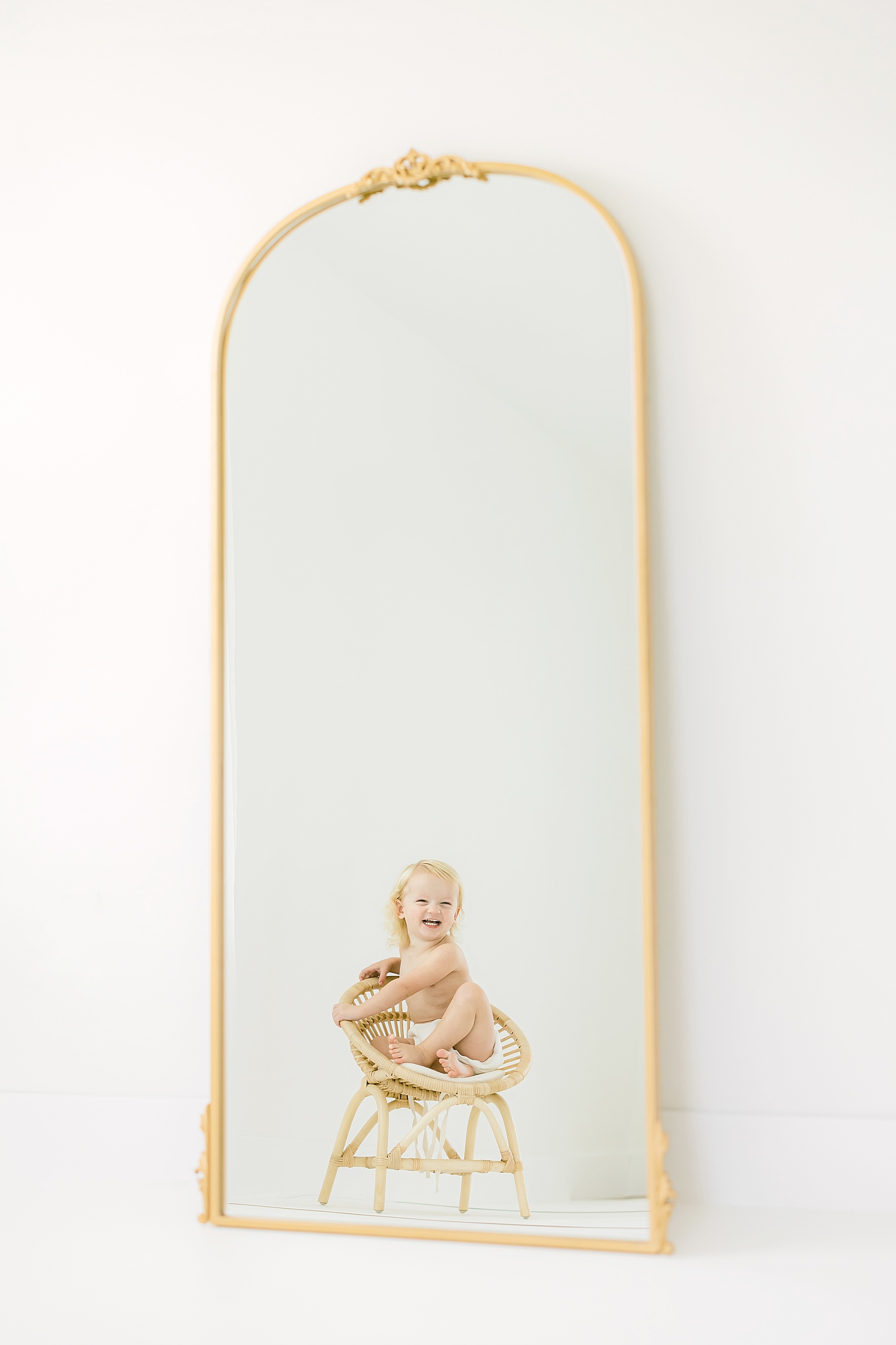 baby boy sitting in rattan chair in front of gold mirror