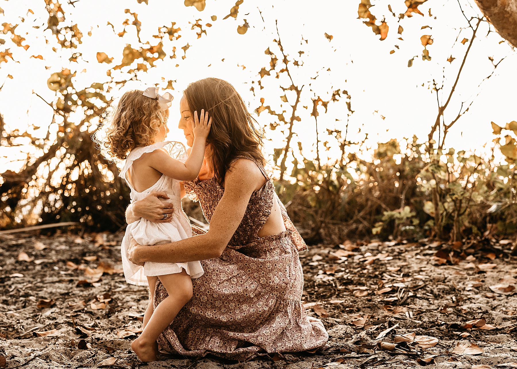 little girl in white dress holding woman in long dress at sunset at the beach