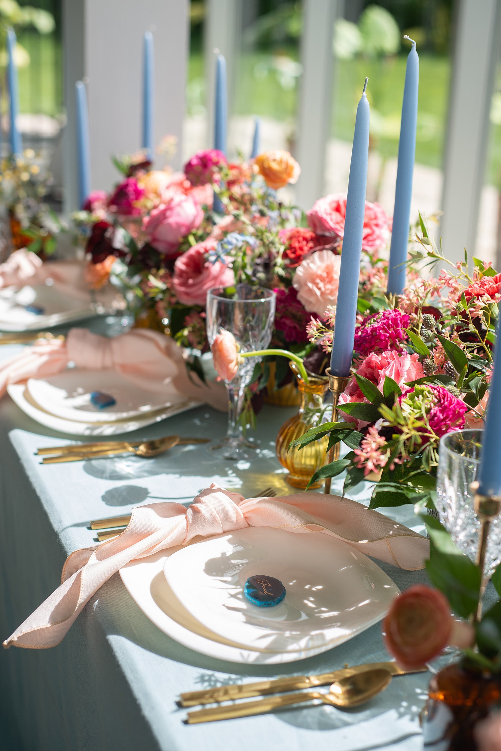 White table setting with gold flatware and colorful flowers at wedding venue.