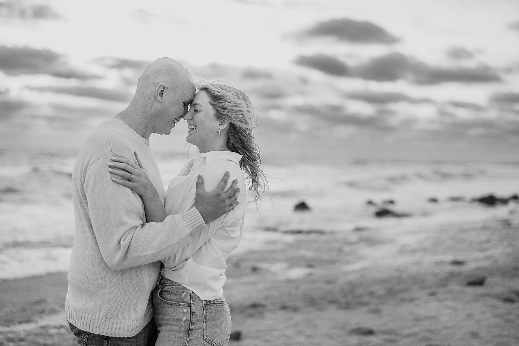 black and white portrait of man and woman holding each other on the beach