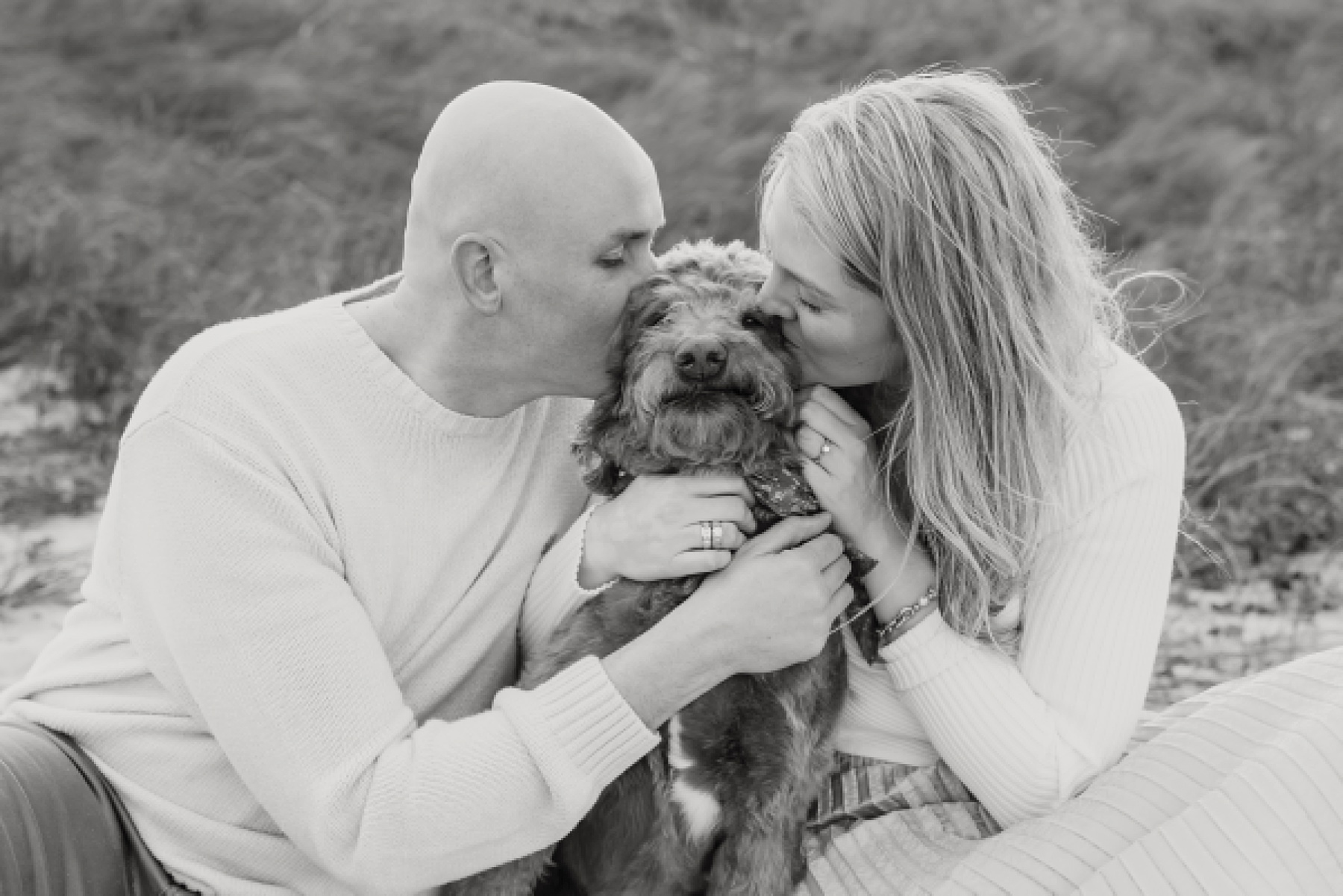 black and white portrait of couple kissing dog on the cheeks