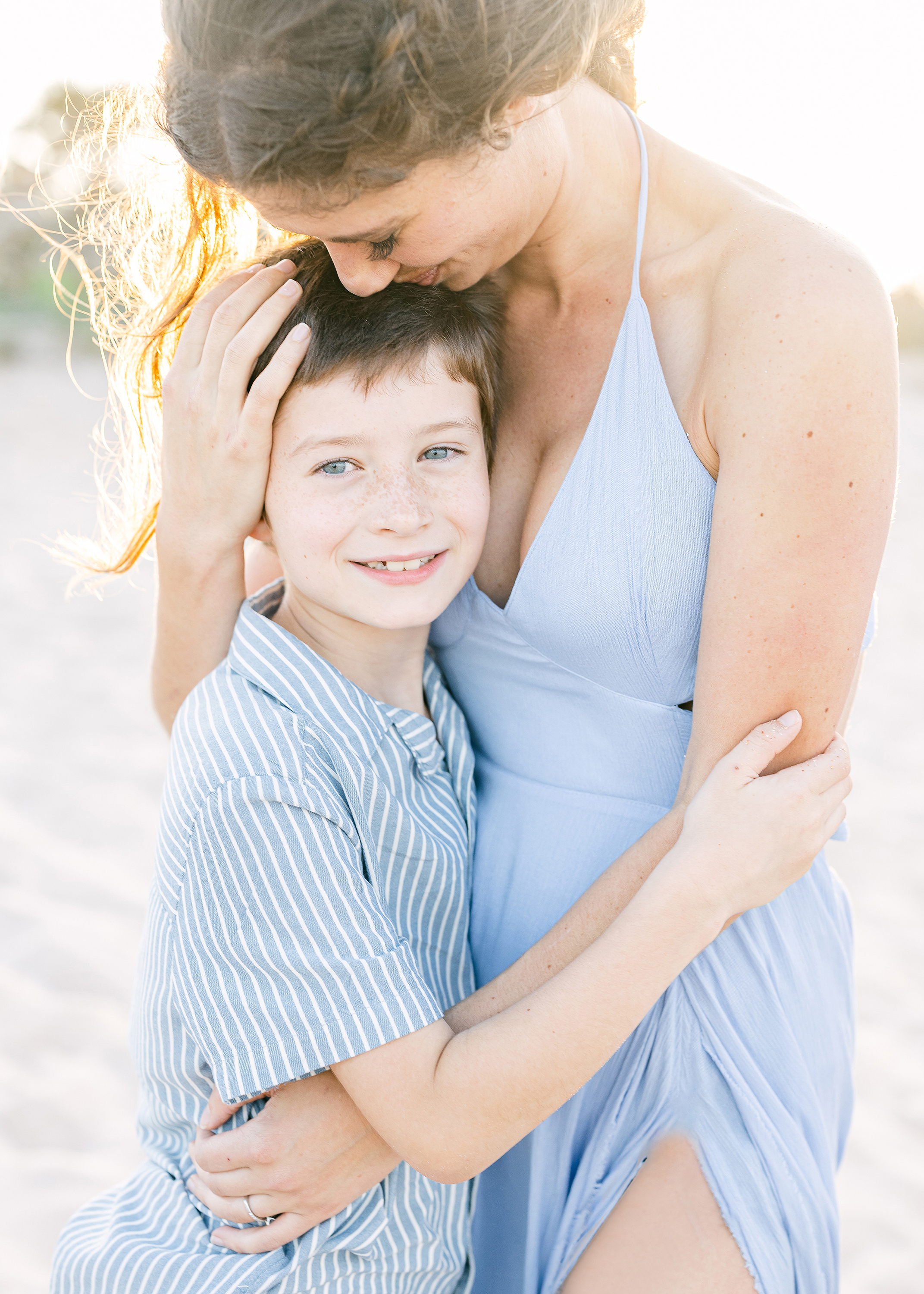 woman in lilac dress kissing little boy at the beach at sunset