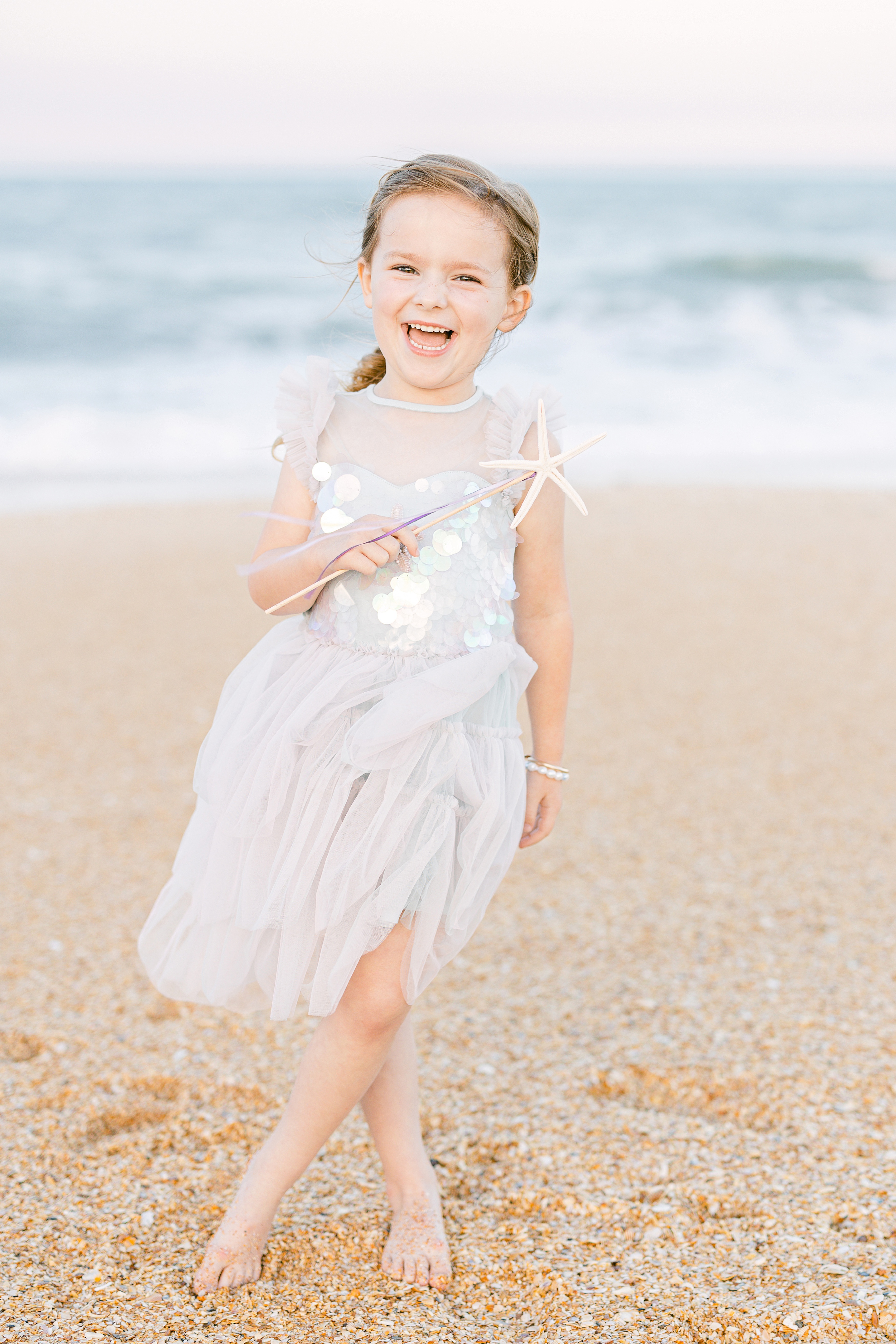 smiling girl with starfish wand at the coastline during sunset