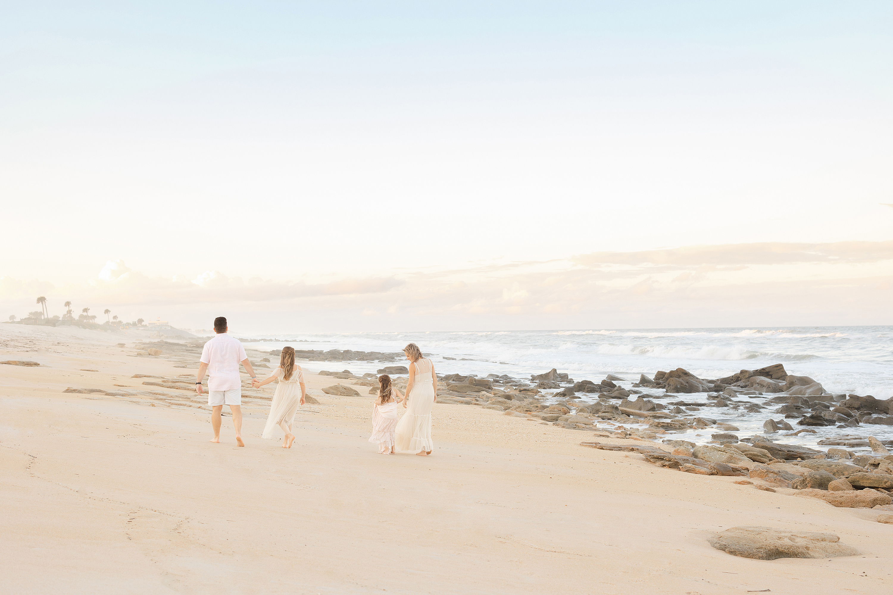 Pastel sunset photo of a family walking on the beach.