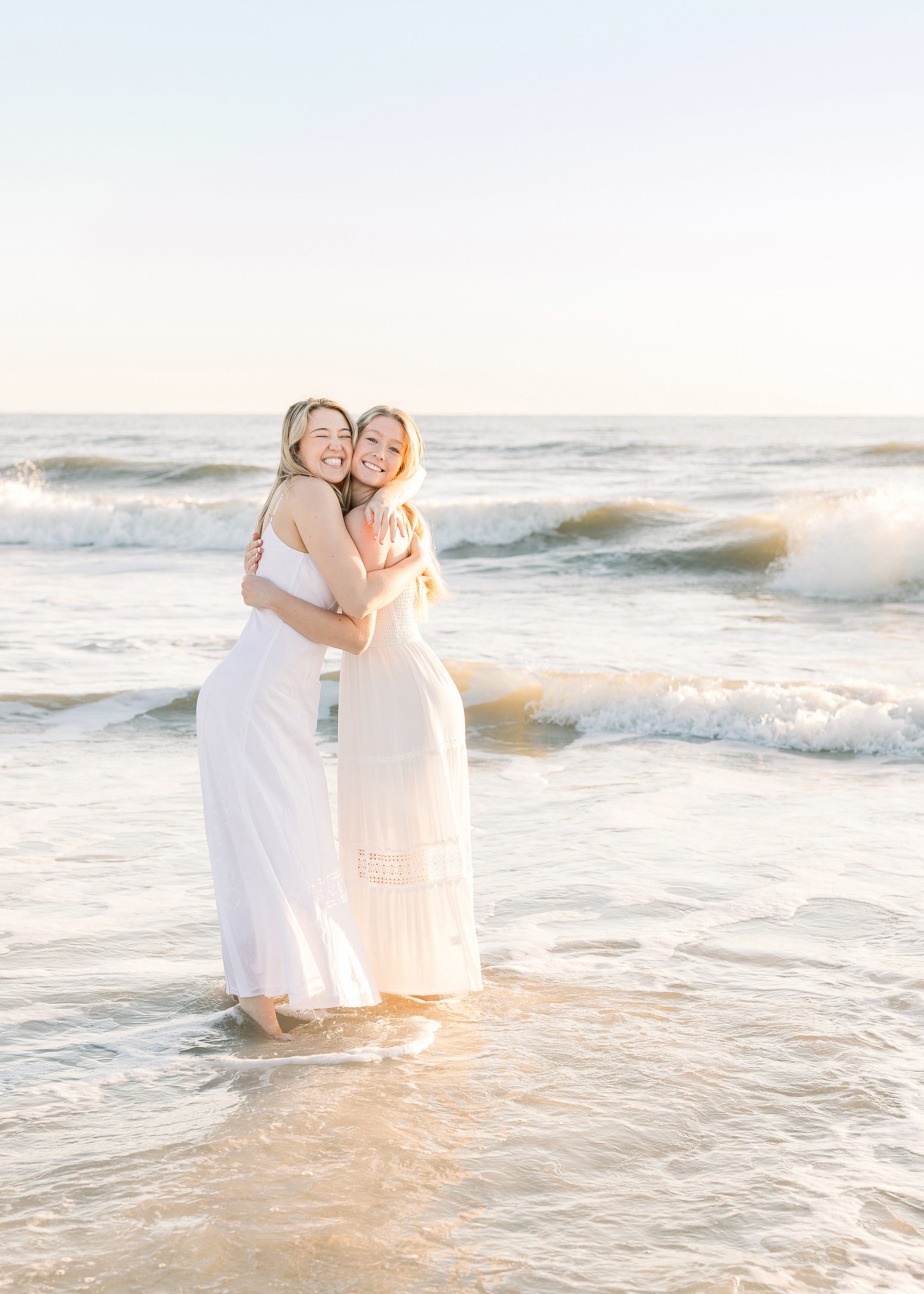 A sunrise beach portrait of two sisters hugging each other in the water.