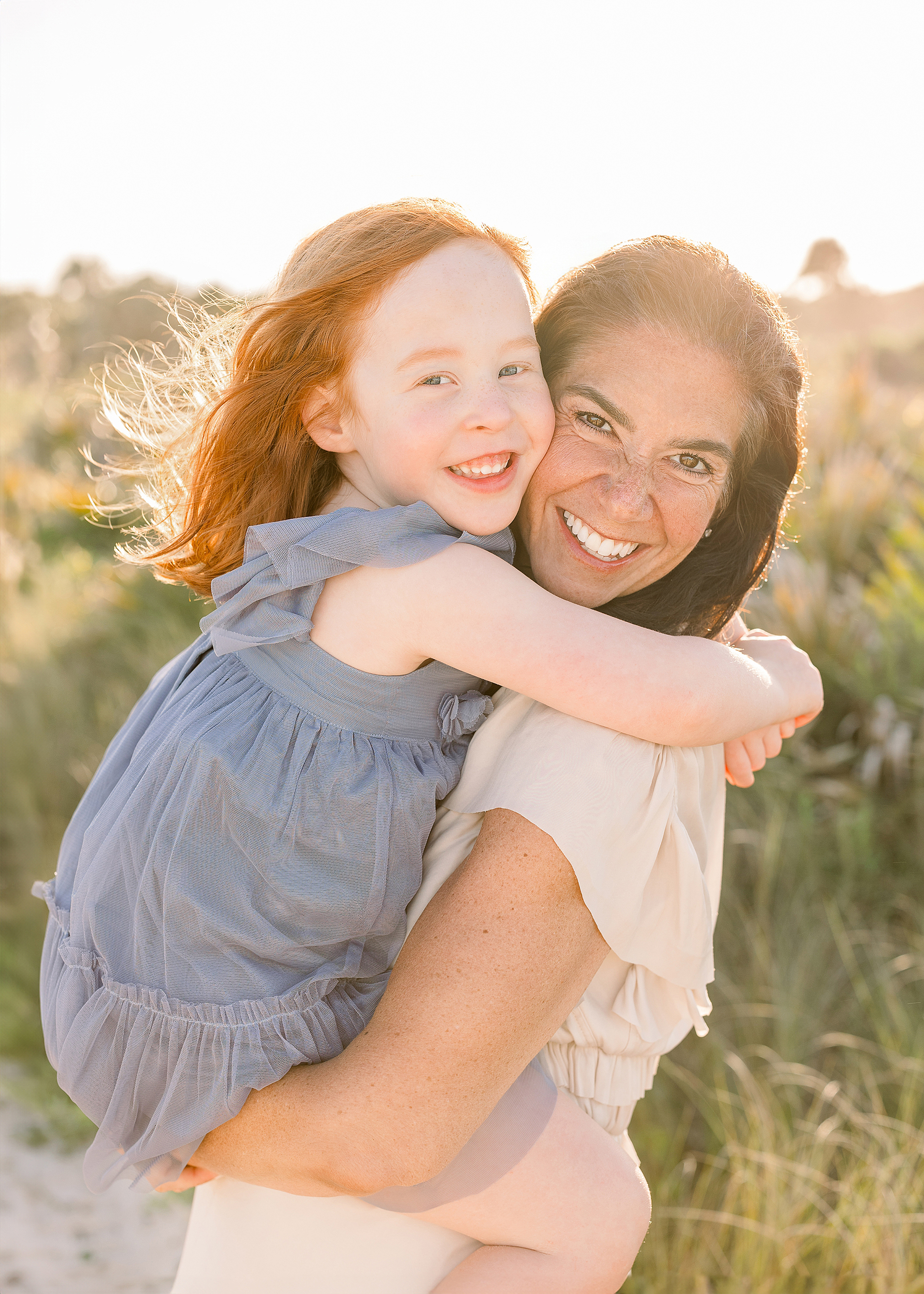 A woman holds her red haired daughter on the beach at sunset.