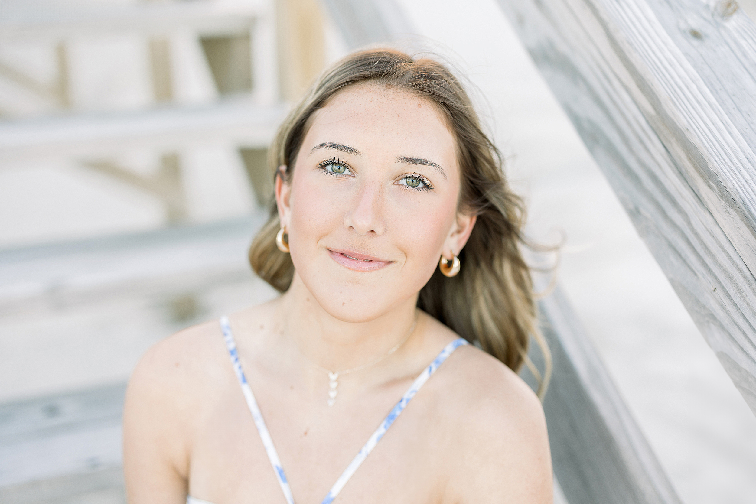 A portrait of a young woman in a blue and white floral dress sitting on the steps at sunset. 