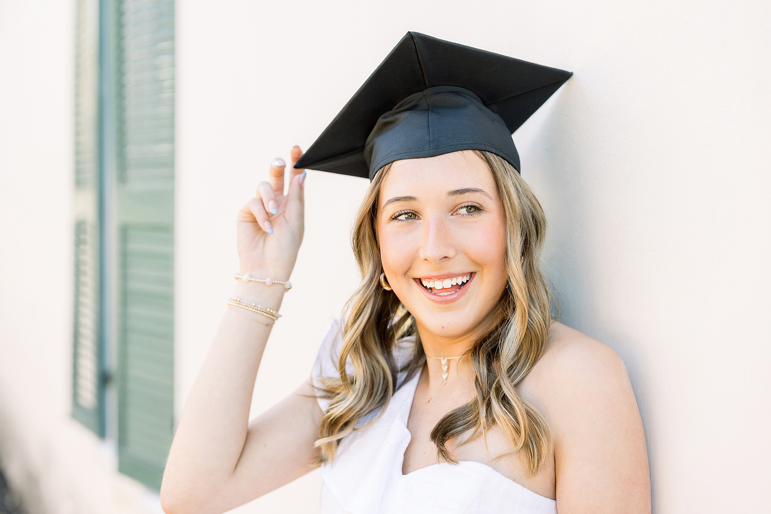 Airy Grad portrait of a young woman in a white dress holding her black graduation cap in downtown St. Augustine, Florida.