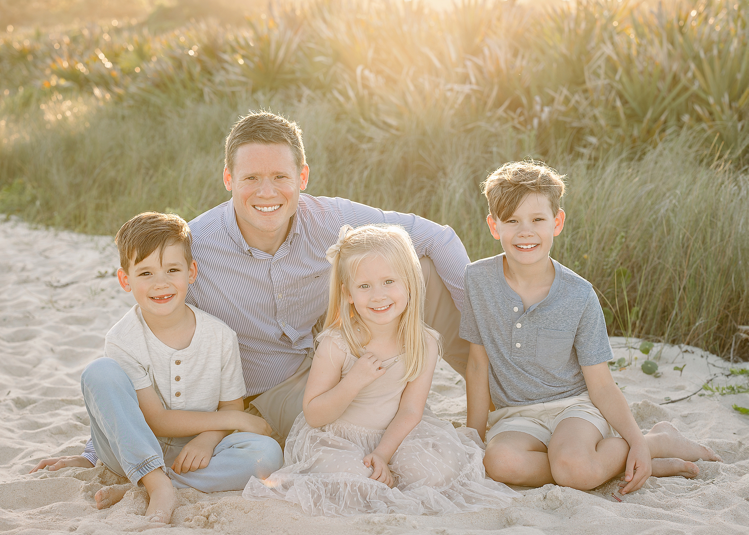 A father with his three children sitting on the sand at sunset on the beach.