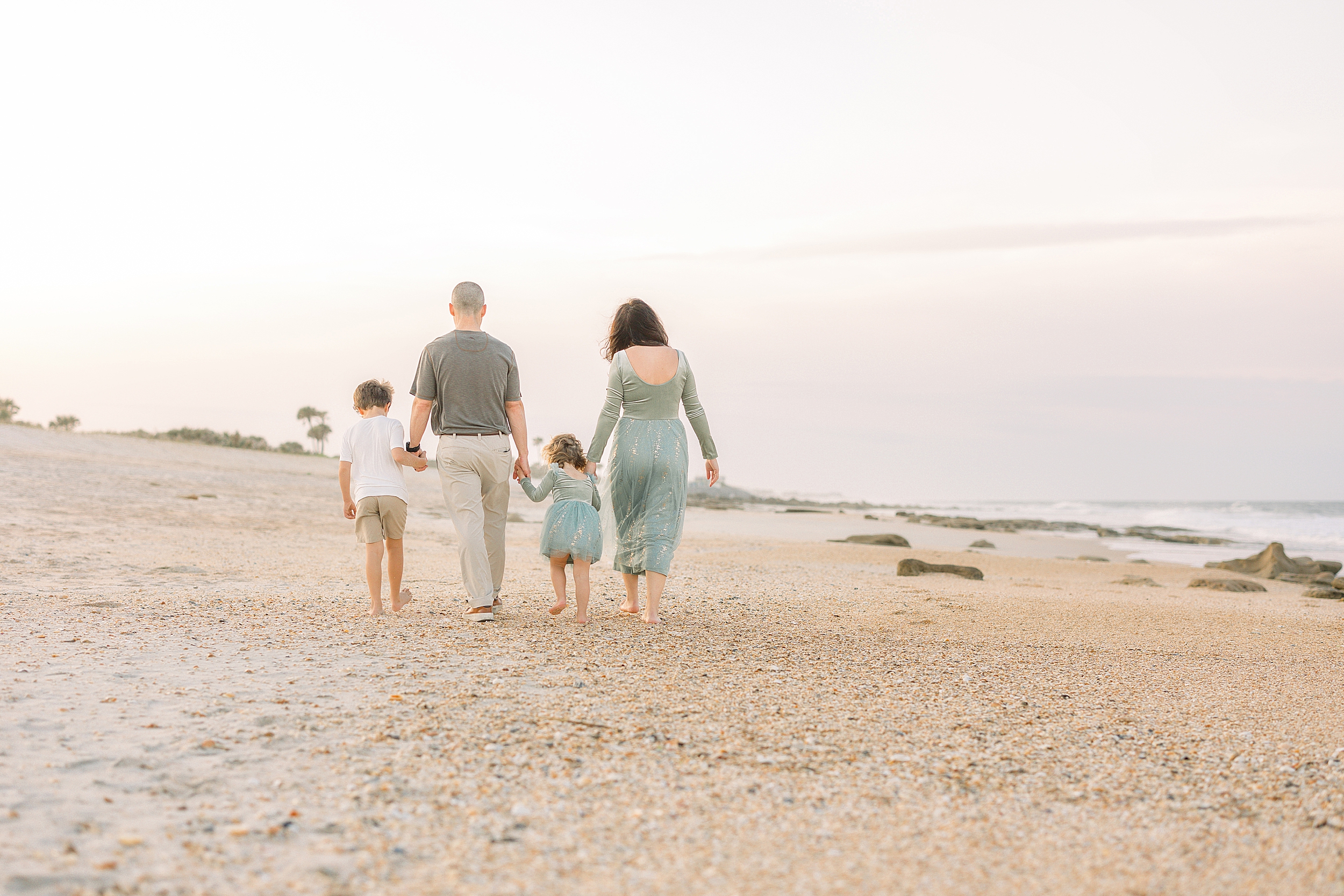 A pastel family beach portrait of a family of four walking on the beach at sunset in St. Augustine Beach, Florida.