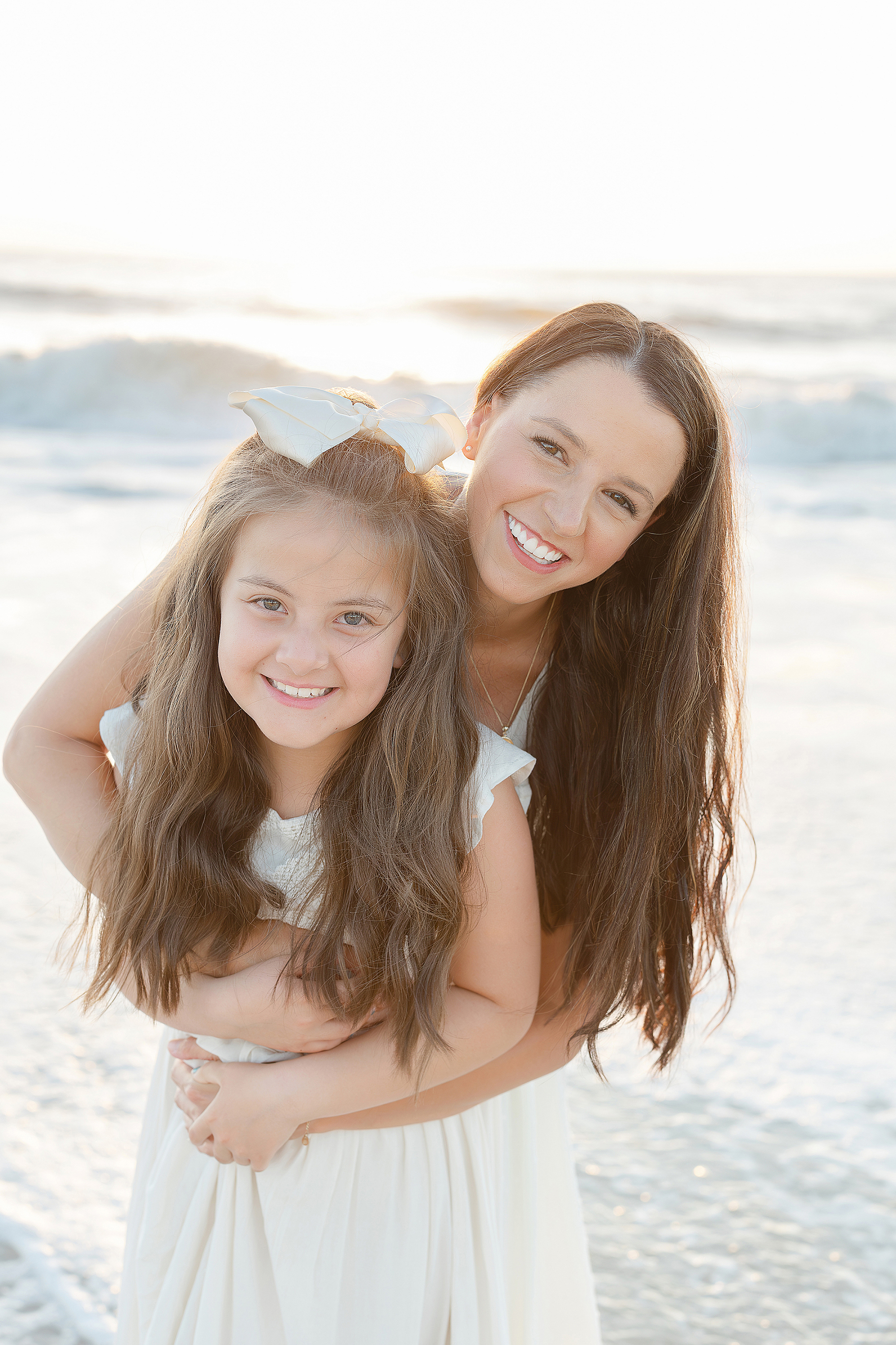 A mother embraces her little girl on the beach at sunrise.