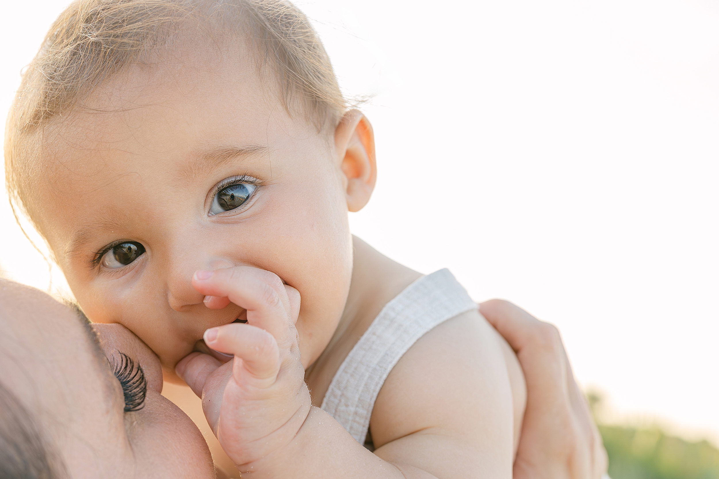 A close up portrait of a baby boy with his mother on the beach.